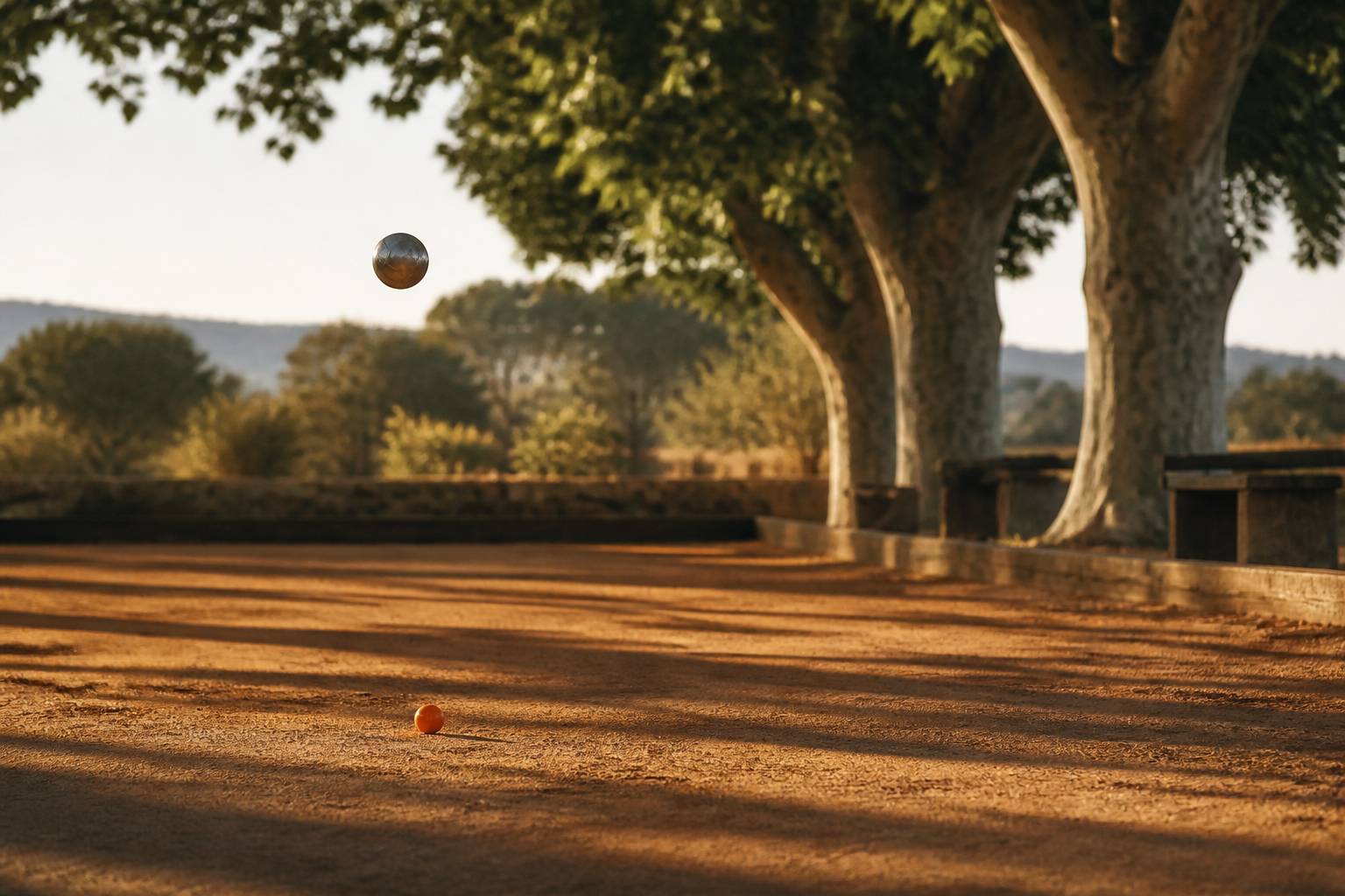 Boule de pétanque en plein vol au-dessus d'un terrain ocre avec le cochonnet au sol