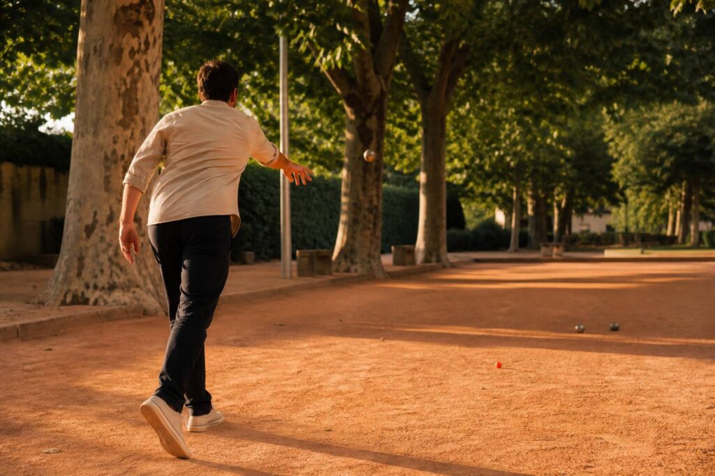 Joueur de pétanque vu de dos lançant une boule en arc au-dessus du terrain