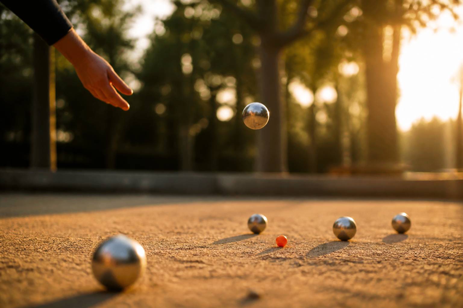 Main lançant une boule de pétanque au-dessus du terrain en fin de journée
