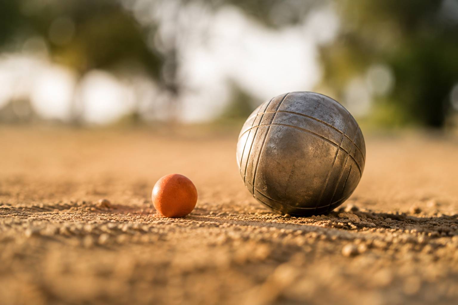 Boule de pétanque striée posée dans la terre battue près d’un cochonnet orange
